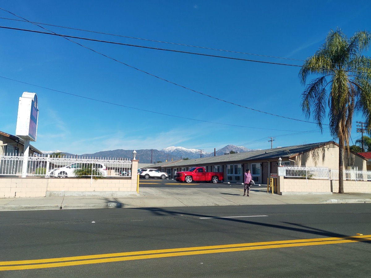 汽车旅馆街景，红色皮卡停在门前，棕榈树与远处雪山