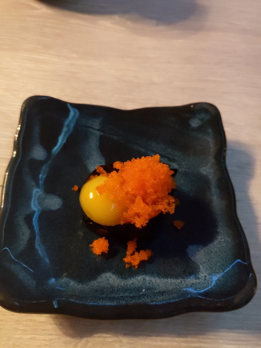 黑陶盘中一枚金黄生蛋黄，堆叠橙红鱼籽，黑色画板衬出撞色