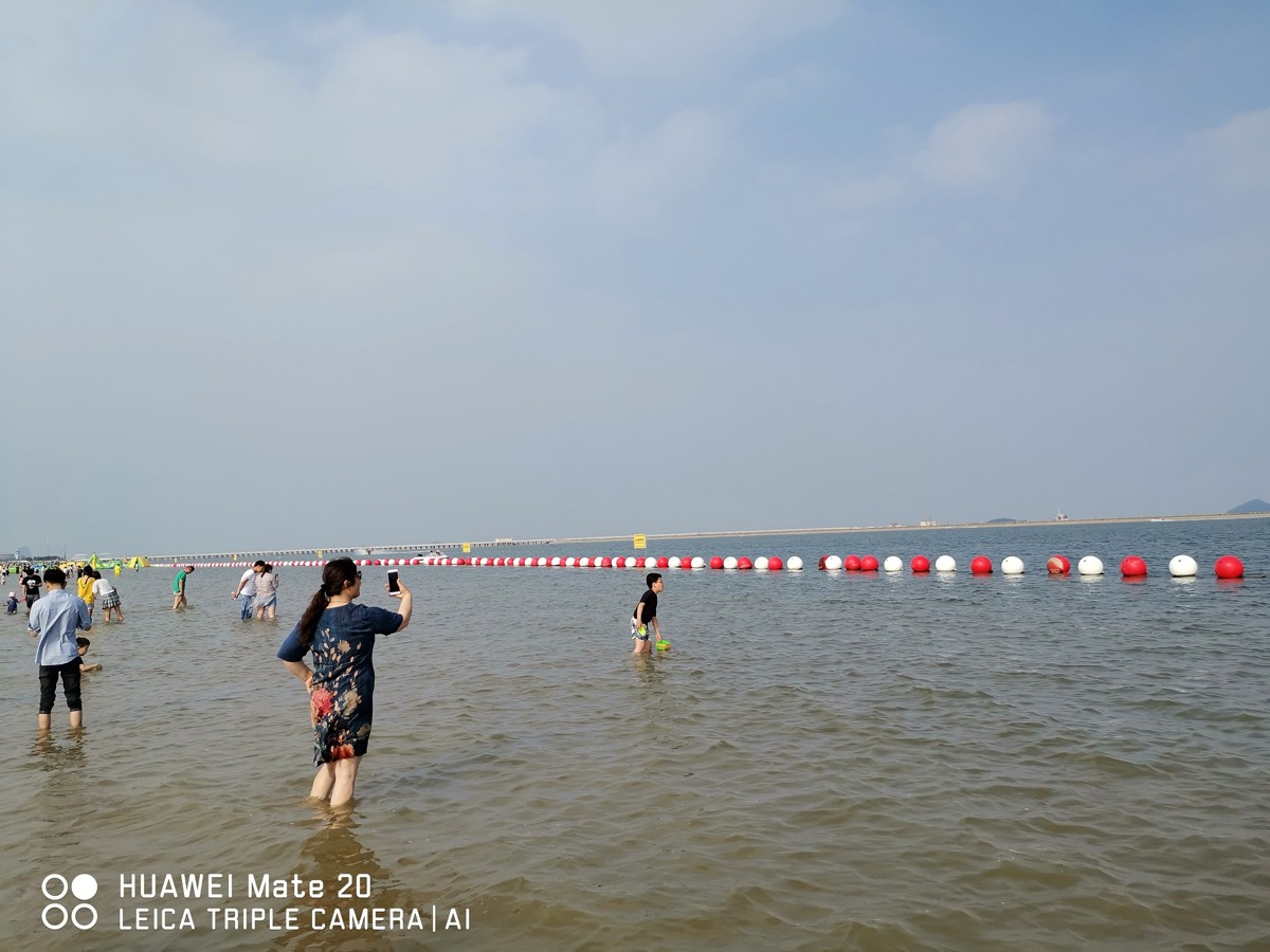 开阔浅海与延伸的红白浮标，家人举手机拍照